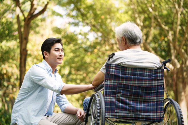 Asian,Son,Talking,To,And,Comforting,Wheelchair,Bound,Father